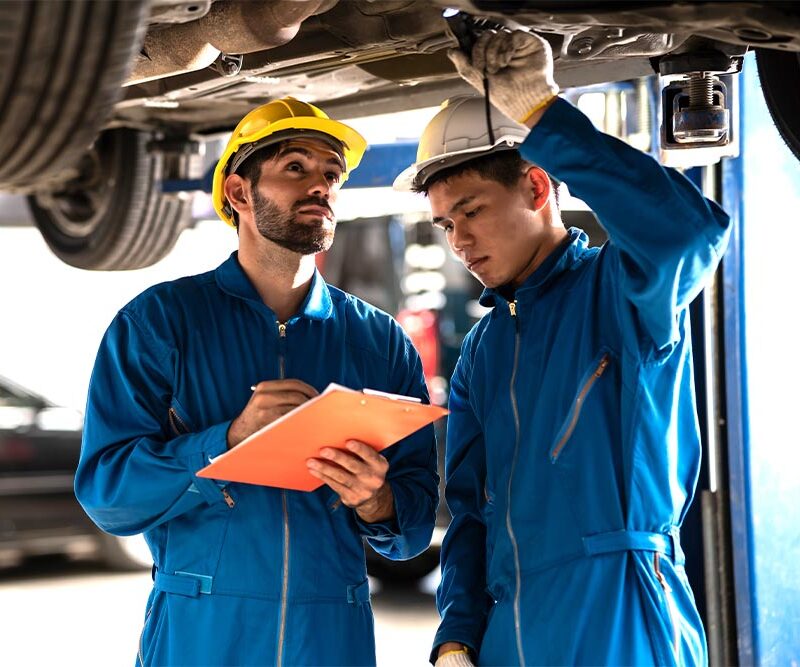 Two professional look technician inspecting car underbody and suspension system by using check list in moder car service shop. Automotive business or car repair concept.
