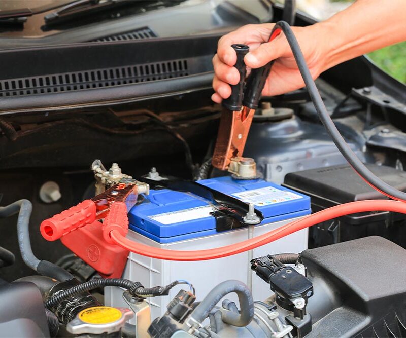 Car mechanic uses battery jumper cables charge a dead battery.